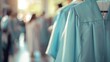 A closeup of a pale blue graduation gown hanging on a coat stand with a blurred background of students mingling and saying their goodbyes. The caption reads The end of a chapter