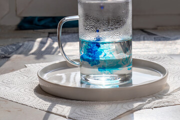 Glass mug with hot water, into which blue food coloring is dripped. Preparation for coloring Easter eggs