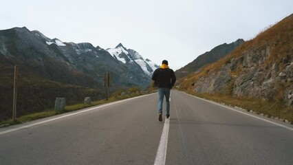 Wall Mural - Man traveler running along a mountain Majestic road Grossglockner Mountain Road in Austria, snow covered sharp peaks of the alpine mountains on background. Incredibly beautiful views in the Alpine
