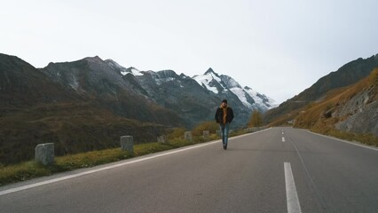 Wall Mural - Man traveler walks along Majestic Grossglockner Mountain Road in Austria, snow covered sharp peaks and glacier of the alpine mountains on background. Incredibly beautiful views in the Alpine mountains