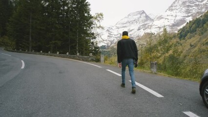 Wall Mural - Man traveler walks along Majestic Grossglockner Mountain Road in Austria, snow covered sharp peaks of the alpine mountains on background. Incredibly beautiful views in the Alpine mountains