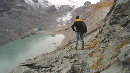 Wall Mural - beautiful young man traveler stands on the observation deck and enjoys the view of beautiful mountains and glacier along Majestic Grossglockner Mountain Road in Austria