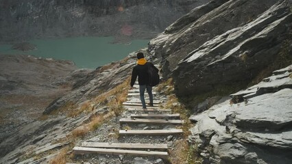 Wall Mural - Young man traveler goes down the path with steps to the glacier enjoys the view of beautiful mountains and glacier along Majestic Grossglockner Mountain Road in Austria