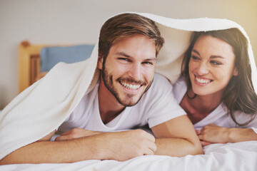 Poster - Smile, love and couple with blanket for relaxing, bonding and resting on bed together at home. Happy, romantic and young man and woman laying with duvet in bedroom at hotel, house or apartment.