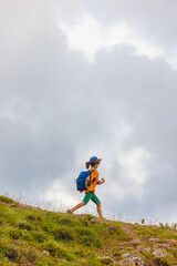 hiking in the mountains. A little boy with a backpack walks along a path against a background of mountains and clouds. Active healthy lifestyle on weekend hike journey.