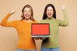 © ViDi Studio - Young friends two IT women they wear orange green shirt casual clothes together hold use work on laptop pc computer do winner gesture isolated on plain pastel light beige background Lifestyle concept