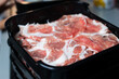 Pork sliced with an automatic meat slicer into round discs, placed in a tray ready to be served with sukiyaki or shabu.