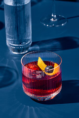 Wall Mural - Popular cocktail negroni with gin and vermouth on blue background with shadow. Negroni cocktail on coloured background in trendy style. Contemporary concept with alcohol beverage. Bartender cocktail.