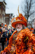 A man with a beard is dressed in an orange costume and matching hat, standing out against the sky at a public event. Dutch event Kings day National holiday Koningsdag on 27 April in the Netherlands