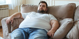 Fototapeta  - Fat lazy adult Man Relaxing on Couch at Home. An unshaven, overweight man with a big potbelly is lying on the couch, infantilized.