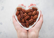 Female hands holding heart shaped plate with peeled pecan nuts on light background.Macro.