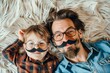 Cheerful father and son wearing matching glasses and mustaches, lying on fluffy carpet