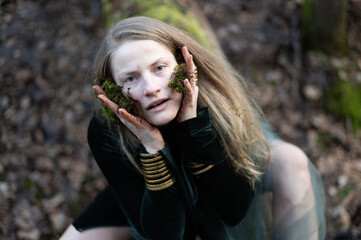 Female shaman performs a nature ritual by smearing her face with forest moss and soil