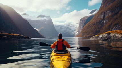 Wall Mural - A tourist on a yellow kayak floats on a lake near the snowy mountains.