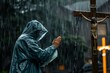 person in raincoat praying by cross during a downpour