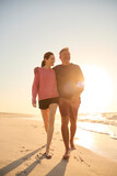 Fototapeta  - Loving Retired Senior Couple On Vacation Walking Along Beach Shoreline Hugging At Sunrise