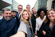 © CarlosBarquero - Selfie of a cheerful team of diverse business people in formal suit looking smiling at camera gathered outside the work building. Positive emotion team work celebrating success together