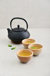 Black cast iron teapot and three ceramic cups of green tea