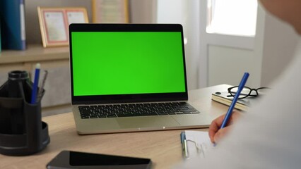 Female doctor writing and watching on laptop computer monitor with green screen,