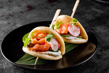 Wall Mural - Delicious gourmet bao buns filled with fresh salmon, radish, and herbs, served on a dark plate, showcasing culinary artistry