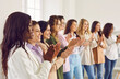 © Studio Romantic - Smiling happy diverse business women standing in a row in office on a grey wall background on meeting or seminar. Group of female multinational company employees applouding at the conference.