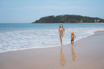 Wall Mural - Beautiful young mother and son running at sea beach in sunny day