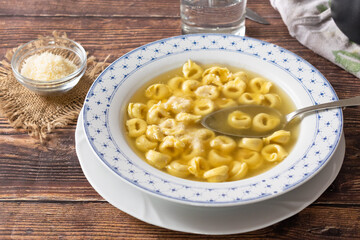 Traditional Italian recipe, Tortellini in broth on a white dish and wooden table.