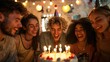 A group of friends gathered around a birthday cake, singing and clapping to celebrate a special occasion. The cake is lit with candles, and everyone looks joyful and festive.