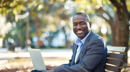 Poster - A man is sitting on a bench with a laptop in front of him. He is smiling and he is enjoying himself