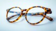 © Sodapeaw - Close-up of stylish tortoiseshell eyeglasses with a detailed pattern, casting a soft reflection on a clean white surface.
