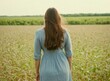© BlackBird Studio - A woman in a dress with long hair standing in a field and looking into the distance. Back view.