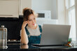 © okrasiuk - Remote work at home. Concentrated young woman working on Laptop at the Kitchen Table in tiny flat apartments. A female student having online classes, Freelancer working from home. Online Job.