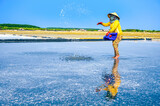 Fototapeta Londyn - A woman is spreading salt to stimulate salt crystallization on her salt field in Can Gio district, a suburban district of Ho Chi Minh City, Vietnam.