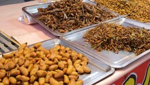 Stall with lots of fried insects (Ma Laeng Tod) include silk worms, waterbugs and grasshoppers and other in outdoor market, slow motion. 