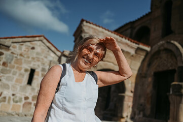 Elderly smiling senior traveling woman backpacker tourist walking posing outdoors in ancient Europe fortress ruins. Retired mature people summer holiday vacation, active lifestyle concept