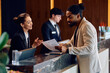 © Drazen - African American man checking in at reception desk in hotel.