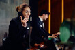 © Drazen - Happy hotel manager talking on phone at reception desk.