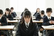 © Bambalino Studio - An asian girl in a school uniform sits at a desk with her head down. The other students in the room are also sitting at desks