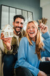 © Jose Calsina - Vertical. couple celebrating a beginning at their new home holding the key of the house. Real estate investment. Mortgage or loan ad. Happy property owners at living room. Married people achievement