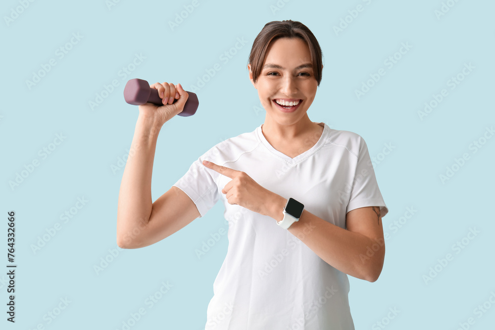 Beautiful happy woman pointing at dumbbell on blue background. Weight loss concept