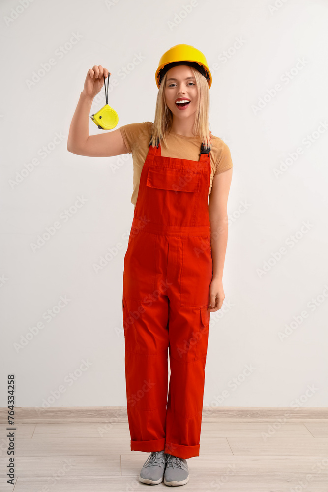 Female worker in hardhat and with tape measure on light background