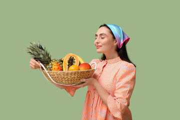 Poster - Beautiful young woman holding wicker basket with exotic fruits on green background