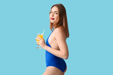 Wall Mural - Beautiful young woman in tank swimsuit and with cocktail on blue background