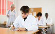 © JackF - Interested young student in white coat listening to lecture and taking notes in classroom during professional medical training