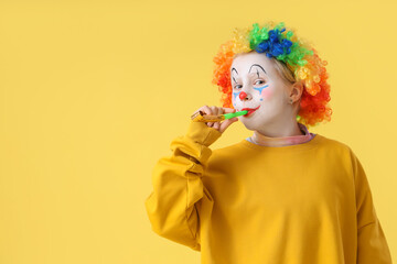 Wall Mural - Funny little girl in clown wig with party blower on yellow background. April Fools' Day celebration