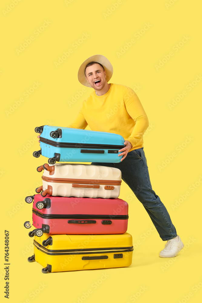 Male tourist with many suitcases on yellow background