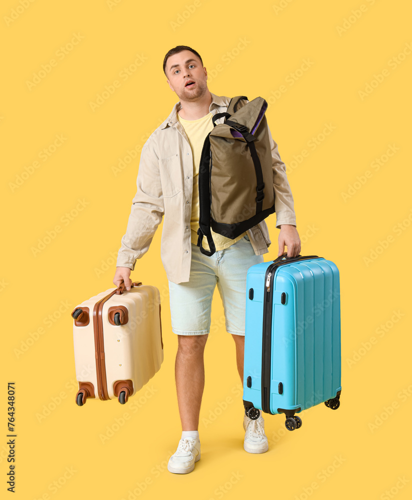 Male tourist with heavy suitcases and backpack on yellow background