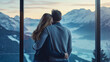 Rearview of man and woman standing hugged, young couple husband and wife looking through the window at beautiful mountain range landscape in the morning sunrise from home interior. Tourism vacation
