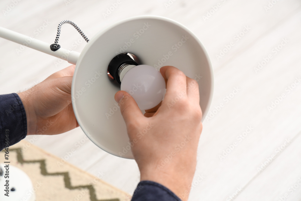 Young man changing light bulb in desk lamp at home, closeup
