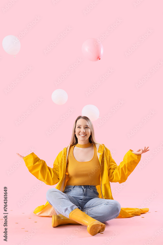 Young woman with balloons sitting on pink background